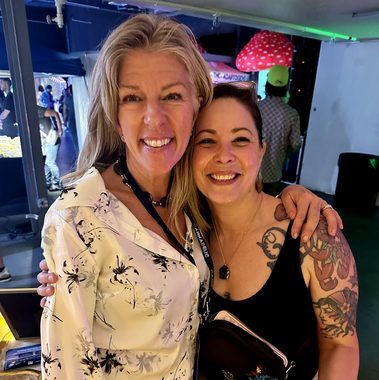 Heather Reilly Hiemstra and a smiling guest pose cheek to cheek at the Cannadelic Night Market, a large red-and-white mushroom installation glowing behind them.