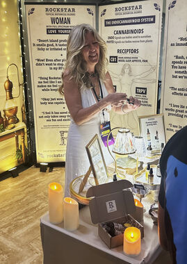 Heather Reilly Hiemstra opens a Rockstar Blends roll-on to demonstrate it at the booth, beside the Rockstar Woman banner and the endocannabinoid-system diagram at Cannadelic Night Market.