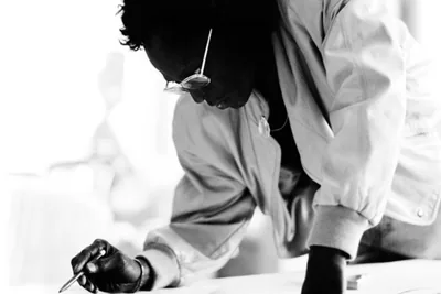 A person bent over a large sheet of paper drawing in bright light