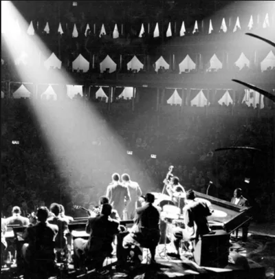 A big band on a concert-hall stage seen from above, a shaft of light across the balconies