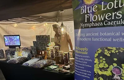 A neighboring vendor's booth at Cannadelic Night Market displaying Blue Lotus (Nymphaea caerulea) botanical products under string lights.