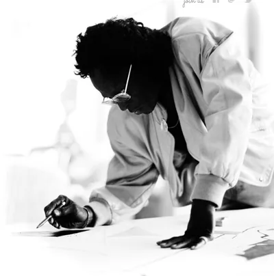 A man in glasses bent over a large sheet of paper, drawing in bright light